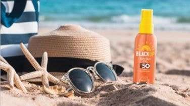 Straw hat, sunglasses and Black Up sun protection lotion on a beach