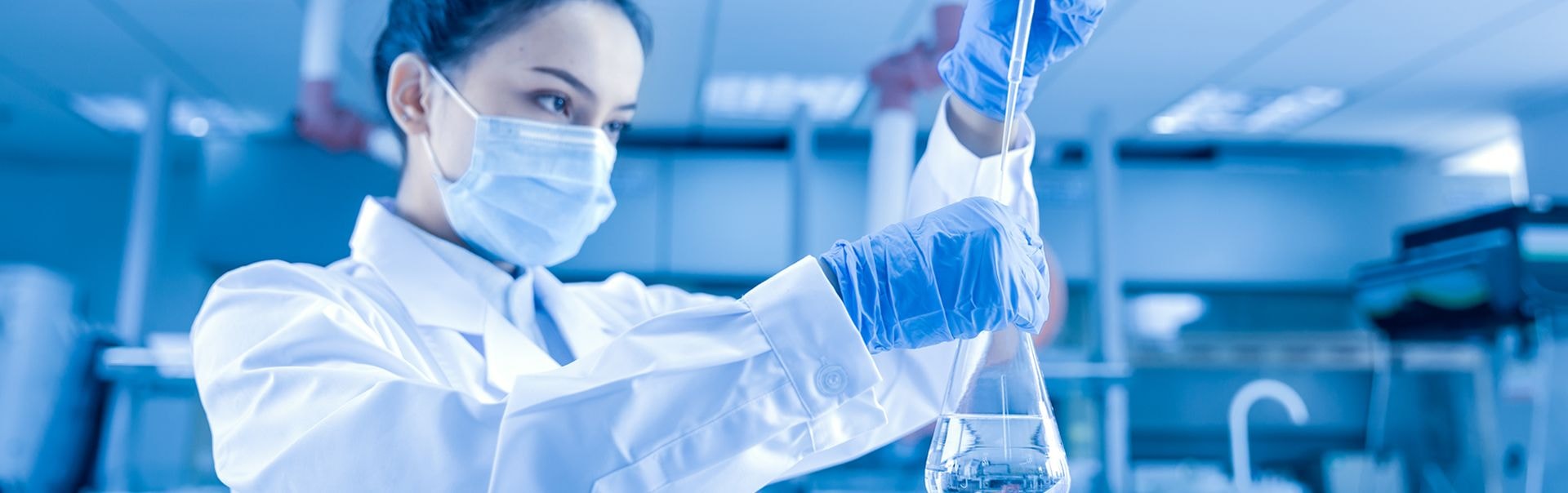 Intern in a laboratory coat and mask working with laboratory equipment