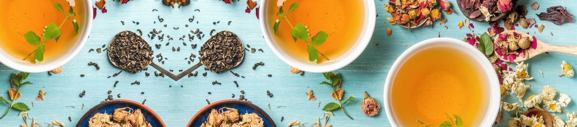 Two cups of herbal tea with dried flowers and herbs on a blue surface