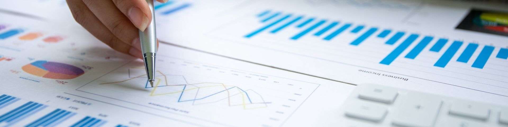 Hand with a pen pointing at printed financial charts