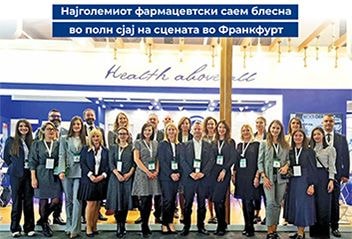 Large group photo of professionally dressed men and women (mostly women) posing together on a trade fair stage, with a "Health above life" banner overhead.