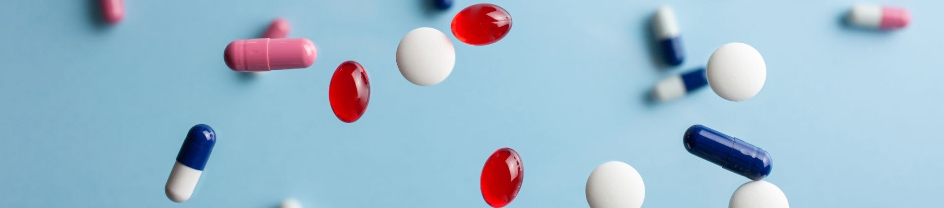 Colourful tablets and capsules falling against a blue background