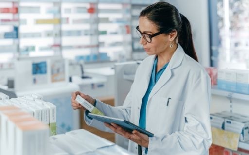 Pharmacist in a white coat reading product packaging in a pharmacy